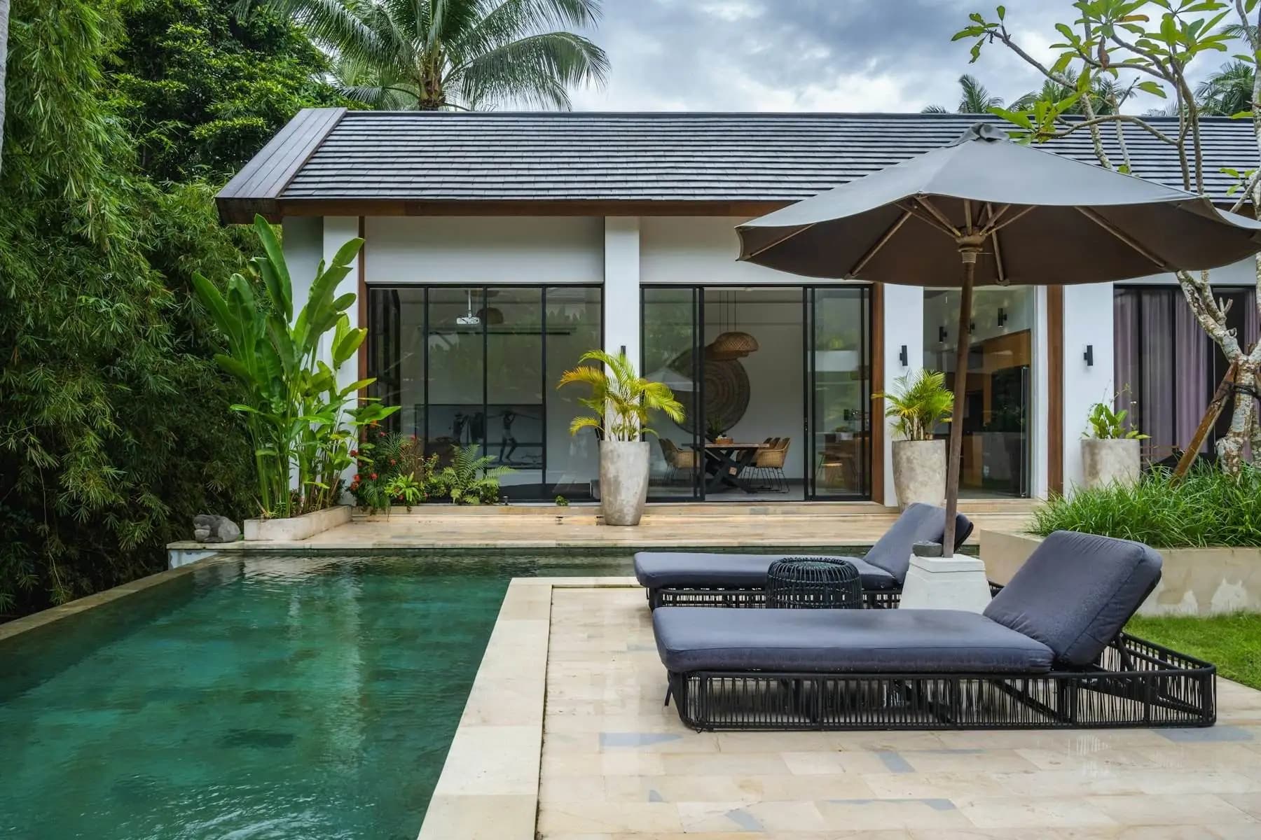 Villa de una planta con piscina, una terraza con tumbonas y un jardín tropical.