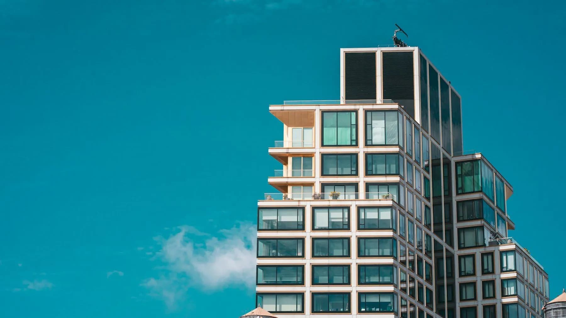 Edificio residencial moderno con balcones y ventanales frente a un cielo azul despejado.